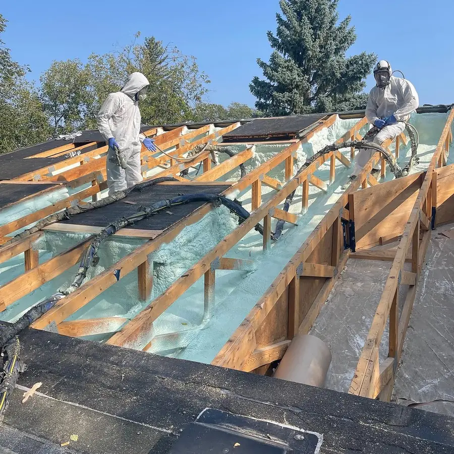 Crew applying closed-cell spray foam insulation between roof rafters